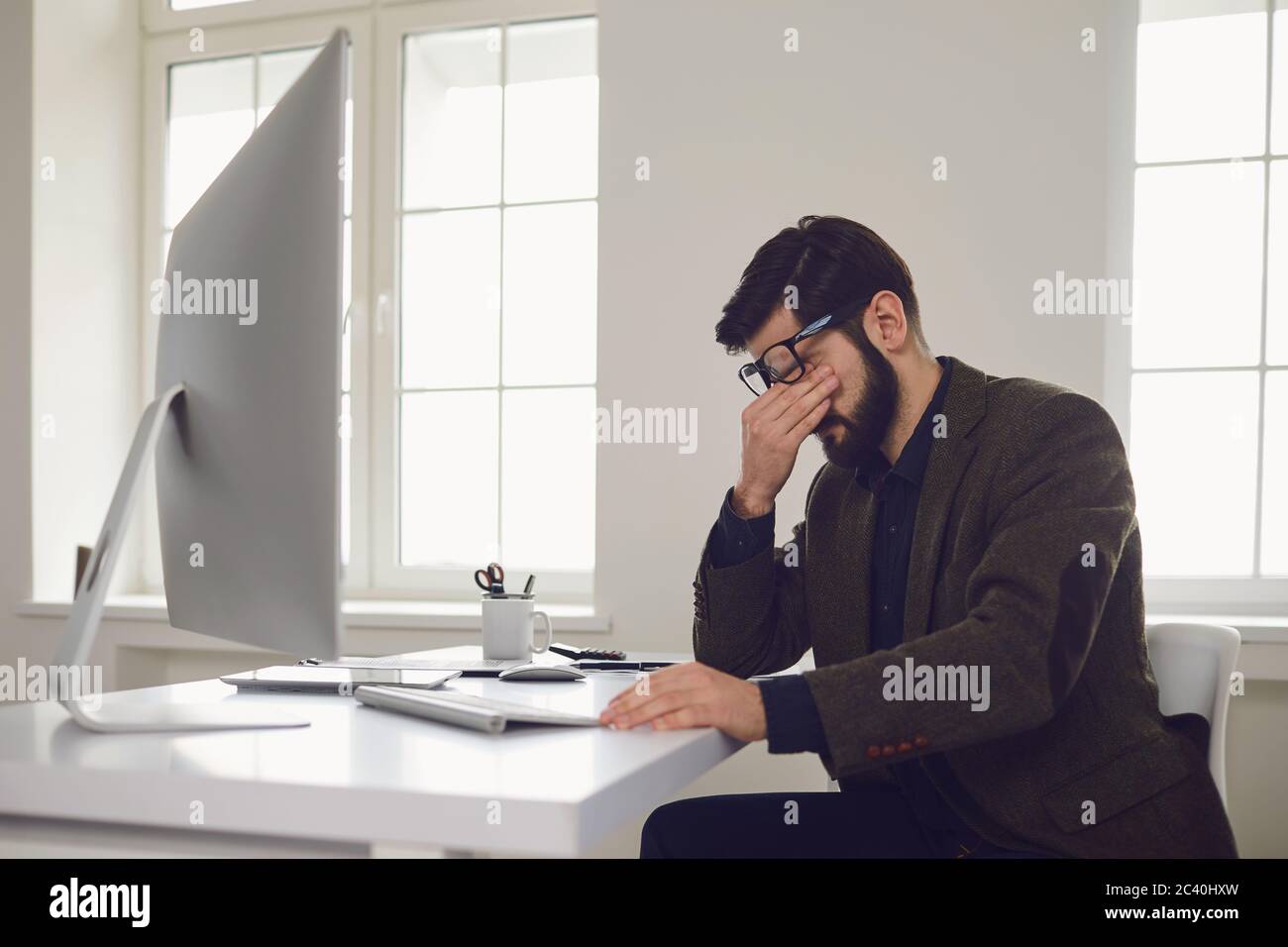 Erschöpfter, müder Arbeiter am Arbeitsplatz bedeckte sein Gesicht mit den Händen im Büro Stockfoto