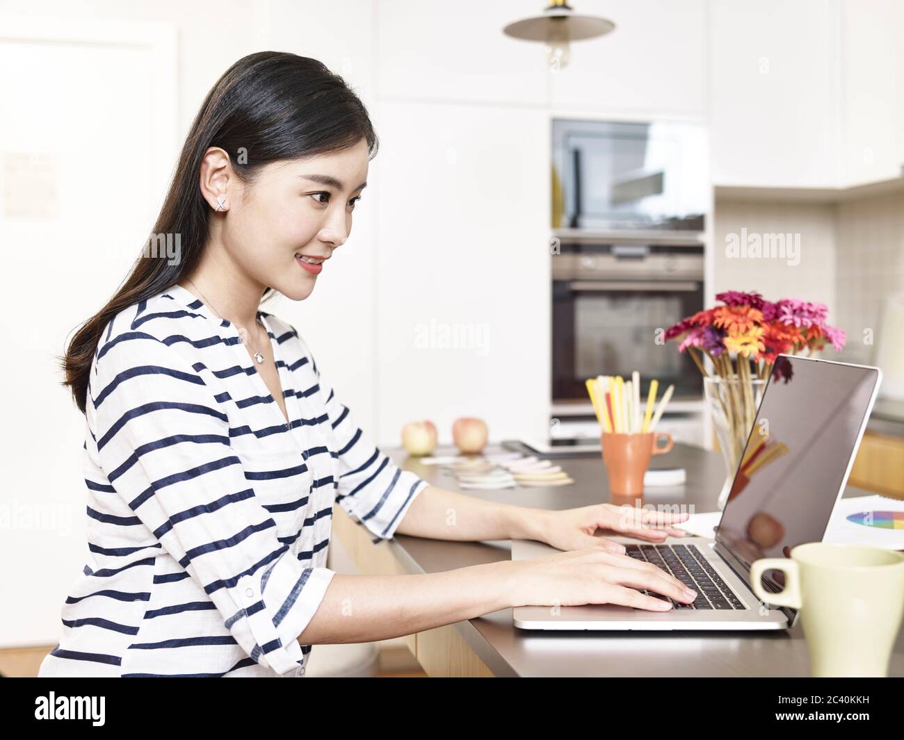 Junge asiatische Geschäftsfrau arbeiten von zu Hause sitzen an der Küchentheke mit Laptop-Computer Stockfoto