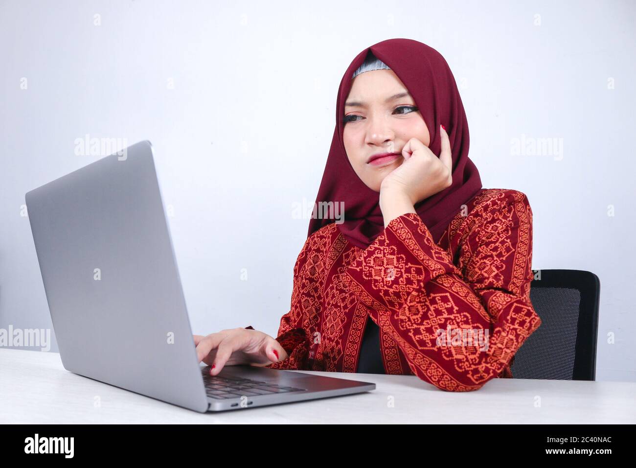 Junge asiatische Islam Frau ist ernst Blick mit denkenden Geste Hand auf Gesicht auf der Vorderseite des Laptops. Stockfoto