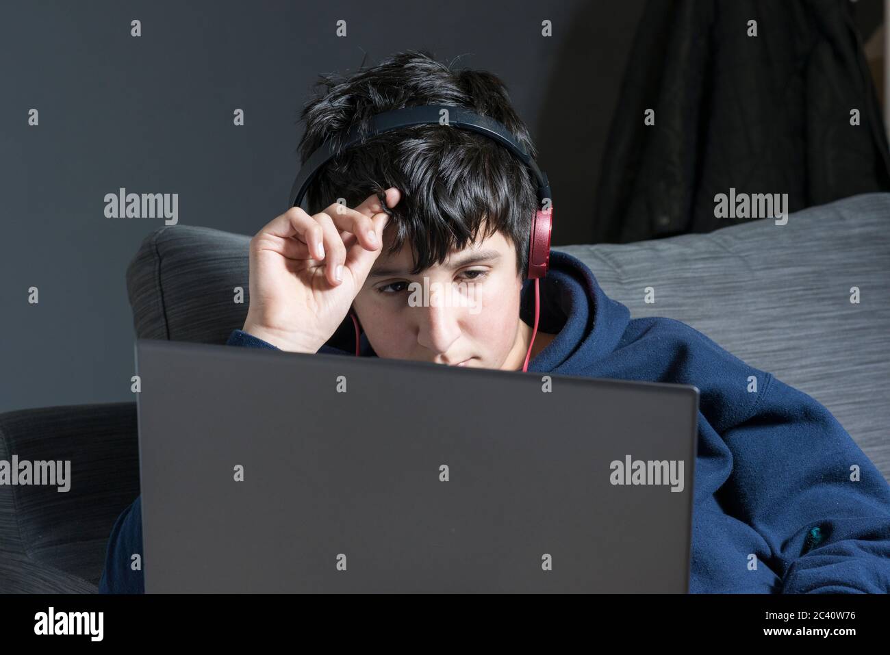 Teenager-Junge trägt Kopfhörer, mit Online-Unterricht- Lernen entfernt während Covid-19 lockdowm, Großbritannien Stockfoto