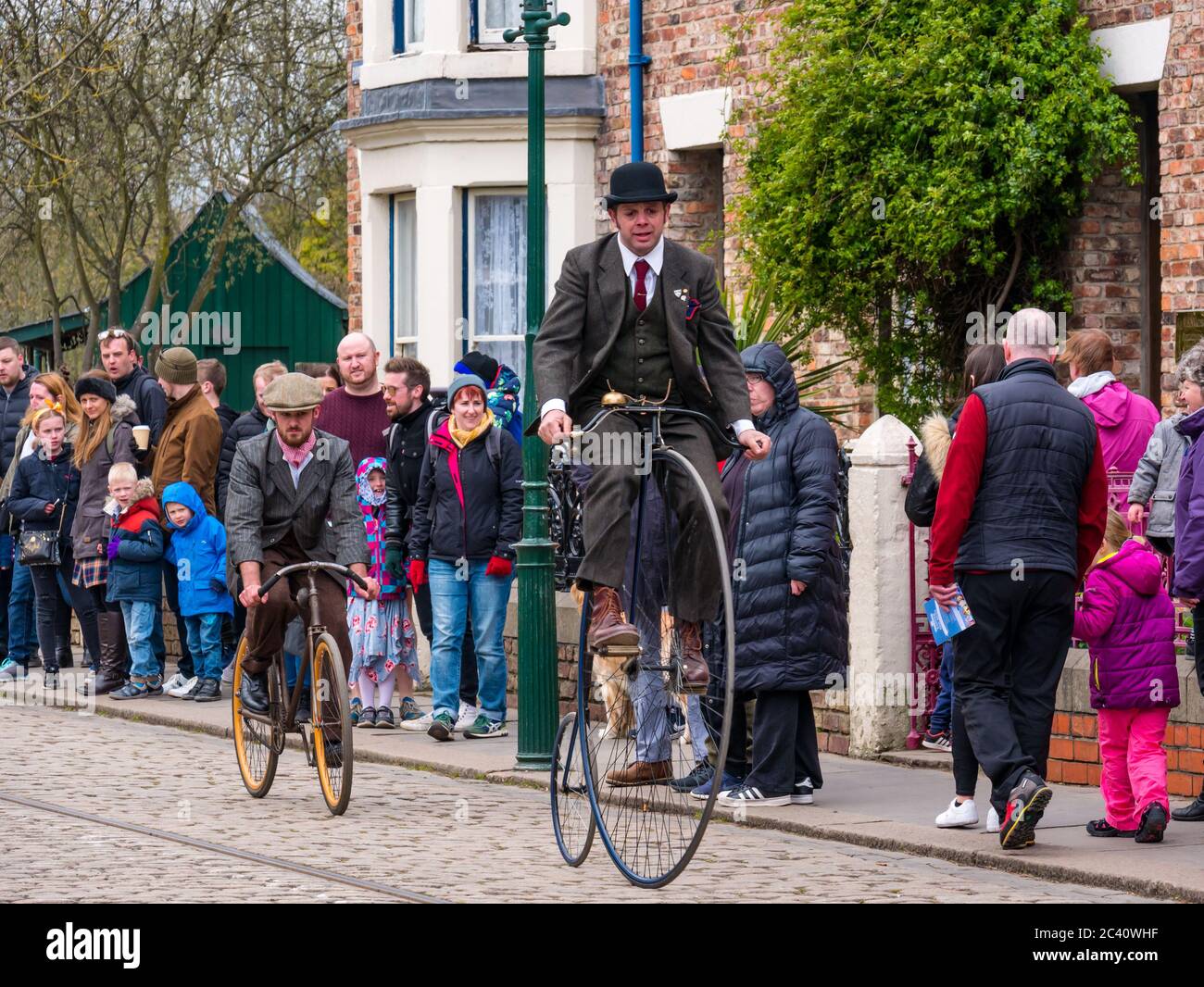 Mann in historischen Kostüm Reiten Vintage Penny Farthing altmodischen Fahrrad in 1900s Stadt, Beamish Museum, Durham County, England, Großbritannien Stockfoto