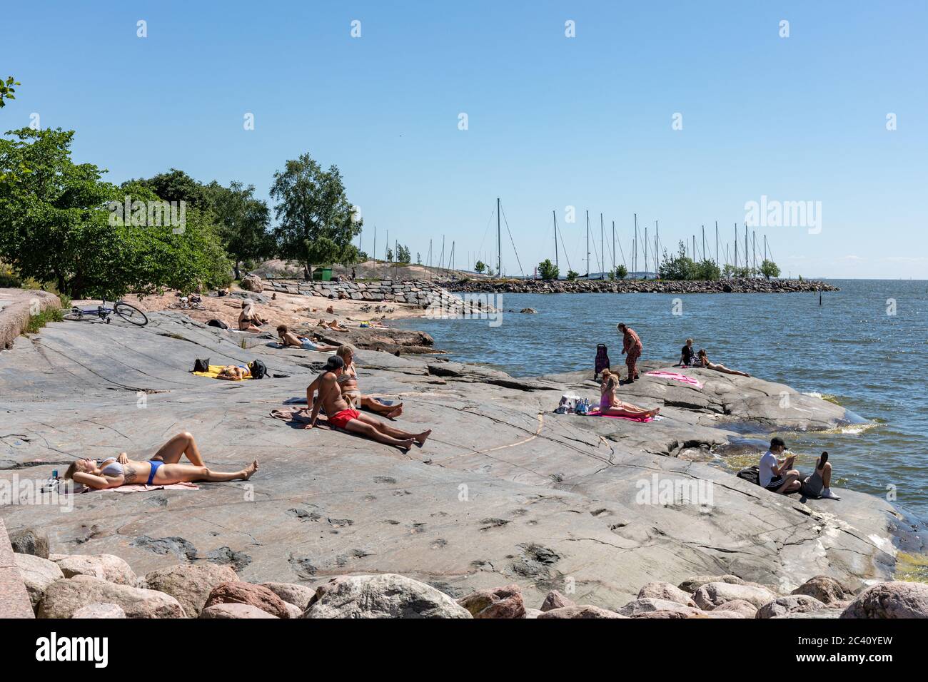 Menschen, die auf einem Felsen am Meer in Eiran Ranta in Helsinki, Finnland, sonnenbaden Stockfoto