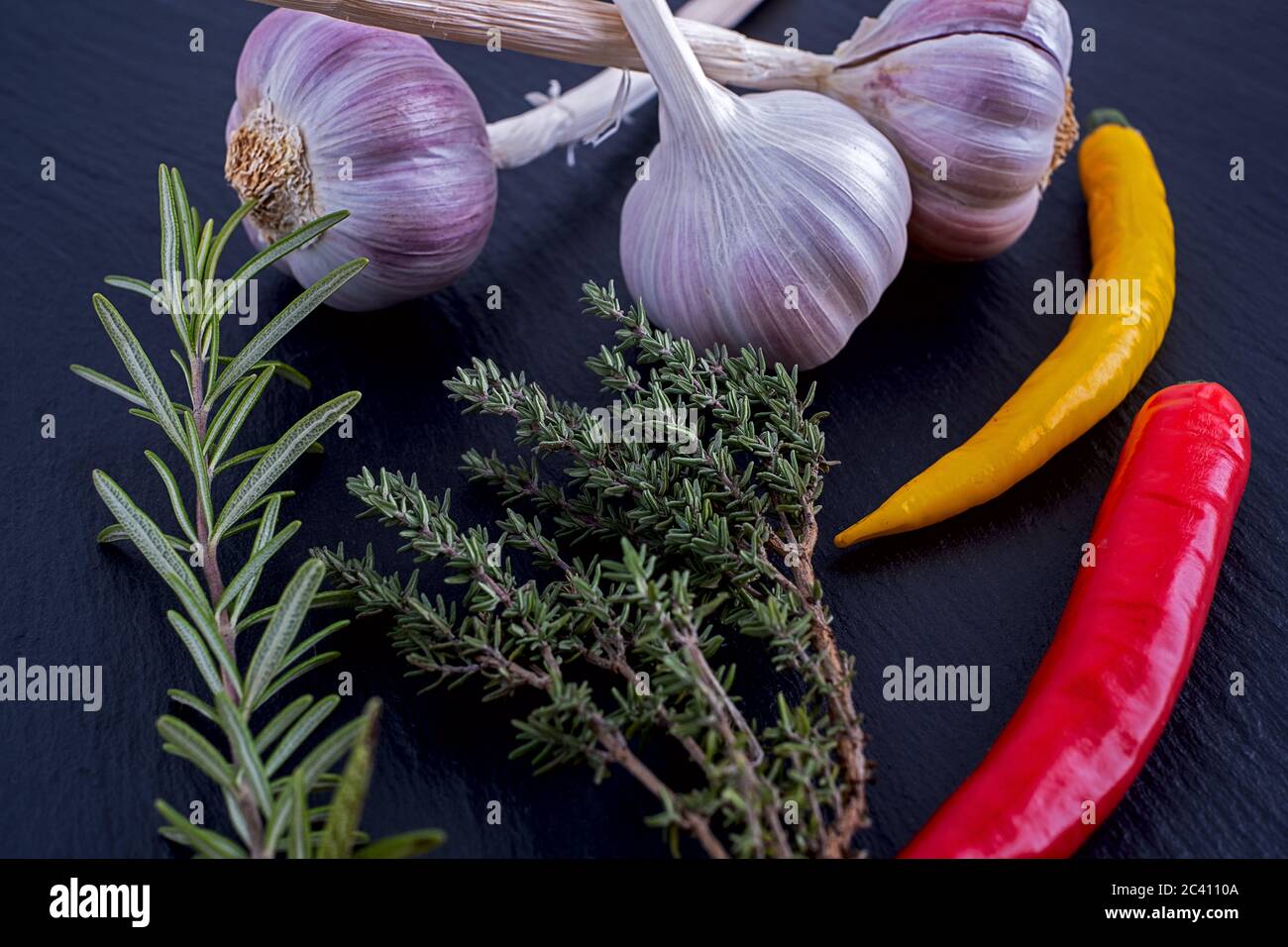 Knoblauch, Rosmarin, Thymian und Chilischoten auf einem Schieferteller Stockfoto