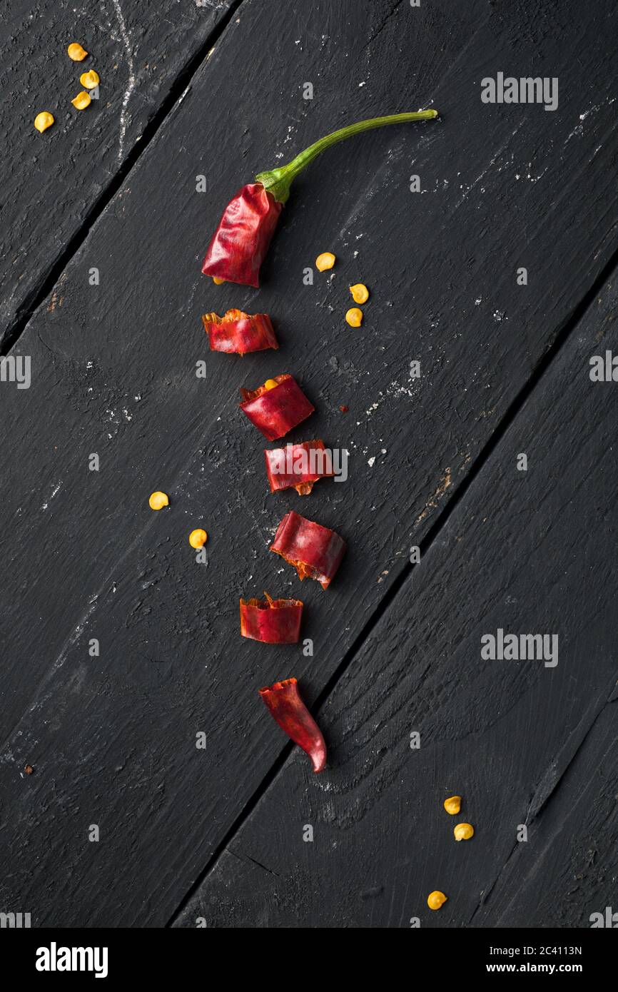 Getrockneter roter Chilischote auf schwarzem Holztisch in Stücke geschnitten Stockfoto