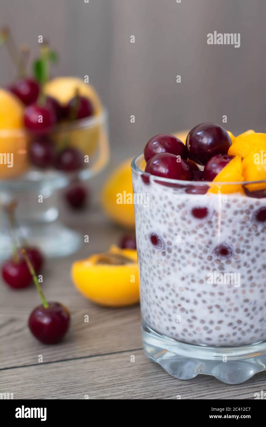 Gesundes veganes Frühstück mit Chia-Samen-Pudding mit frischen Aprikosen und Kirschen. Mehr Obst und Vintage Silber Löffel im Holzhintergrund. Stockfoto