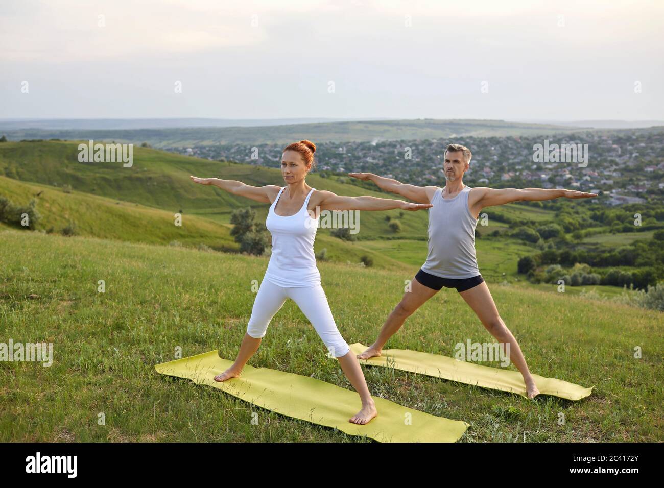 Ein Mann und eine Frau praktizieren synchron Yoga, meditieren Gleichgewicht in der Pose des stehenden Grases auf der Natur. Stockfoto