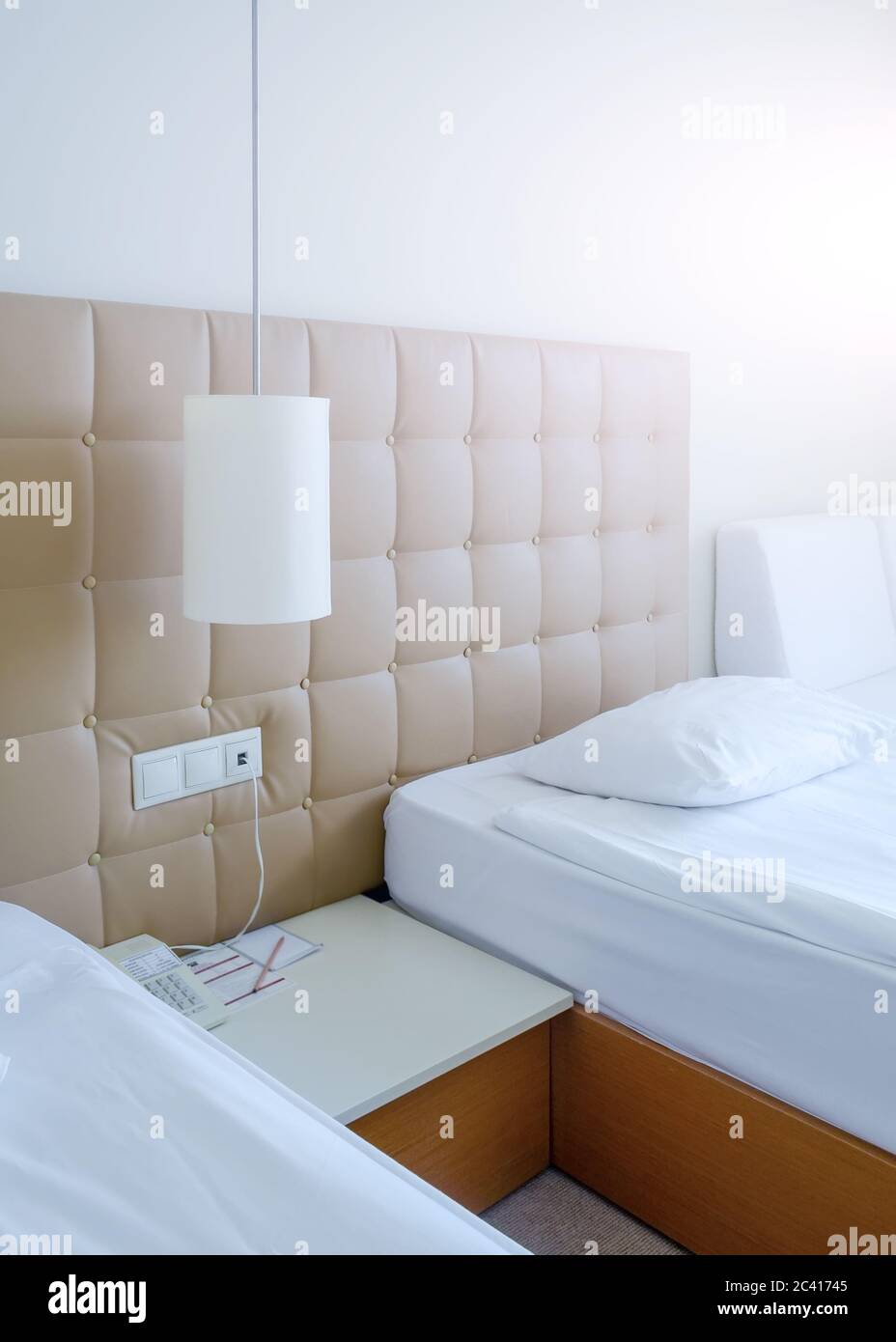 Helles Zimmer in einem Hotel in hellen Farben mit zwei Betten, Nachttisch und Lampe Stockfoto