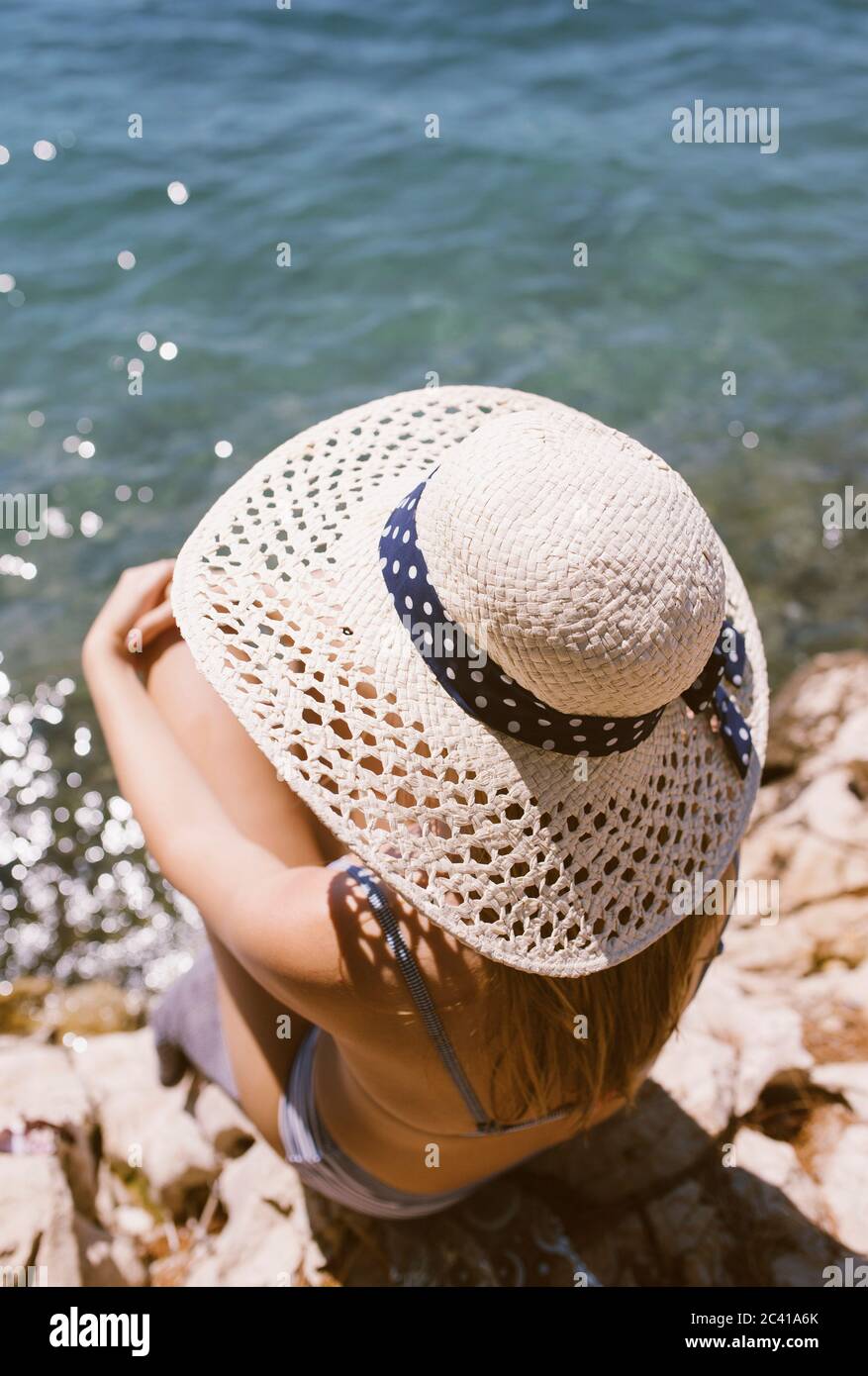 Frau mit Hut sitzt am Strand am Meer Stockfoto