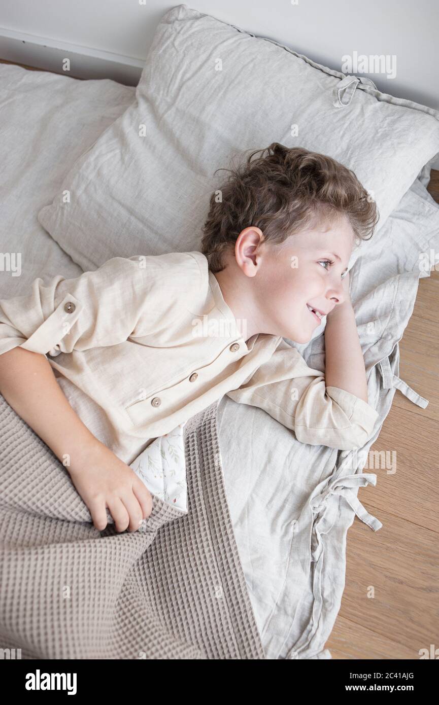 Junge in Hauskleidung liegt freudig in natürlichen Betten nach dem Aufwachen. Stockfoto