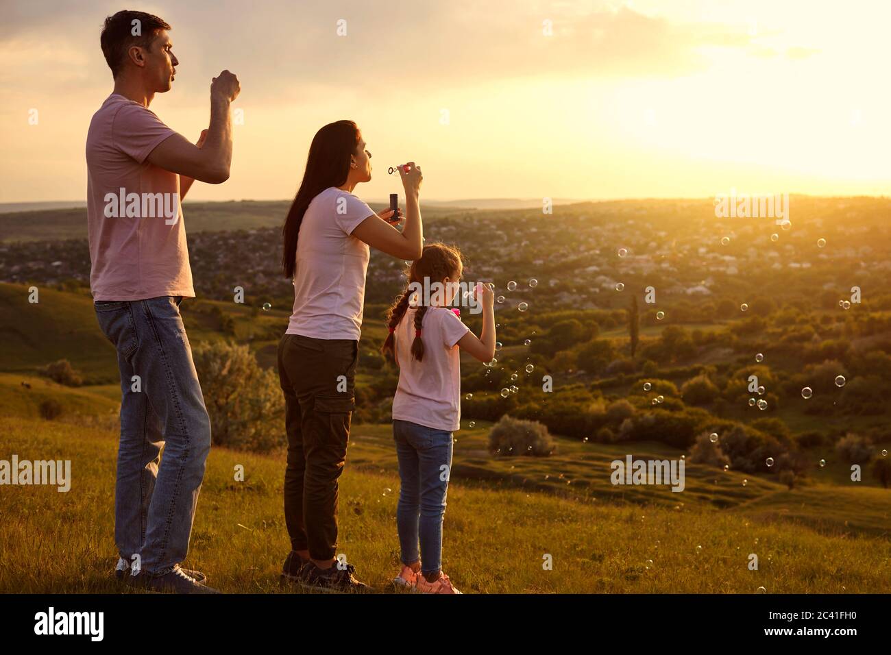 Liebevolle Familie mit Spaß Seifenblasen auf Berggipfel bei Sonnenuntergang. Eltern und Kind spielen zusammen Stockfoto