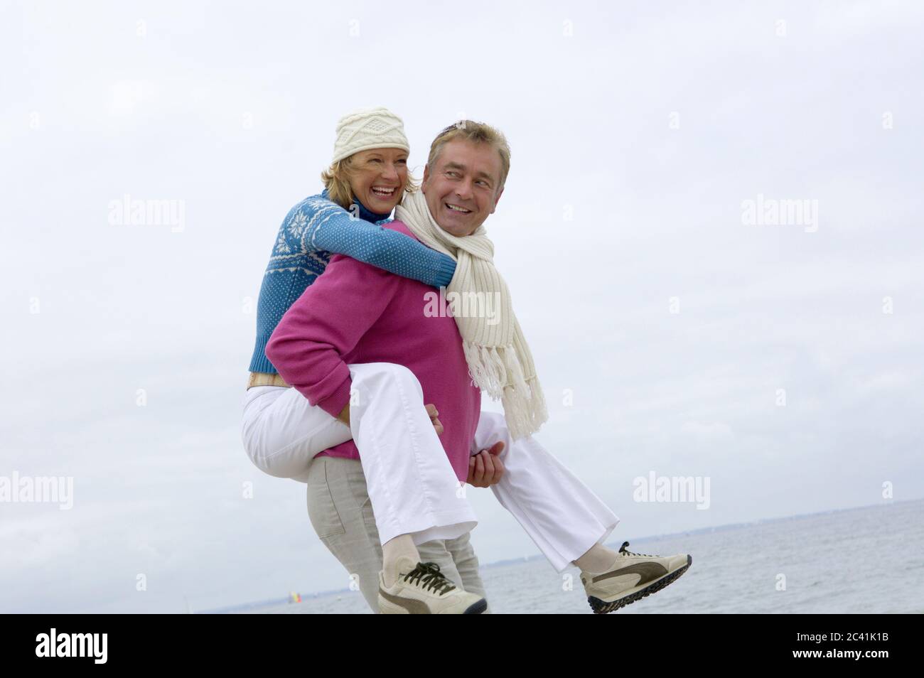 Älterer Mann trägt Frau Huckepack am Strand Stockfoto