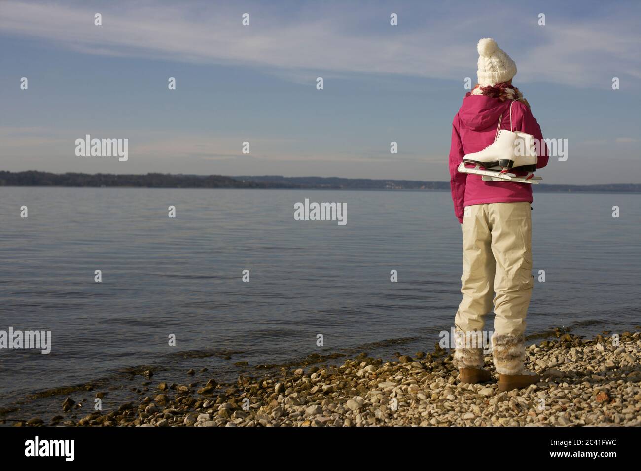 Frau in Winterkleidung mit Schlittschuhe unter einem blauen Himmel vor einem See - Wetter - Saison - Wintersport Stockfoto