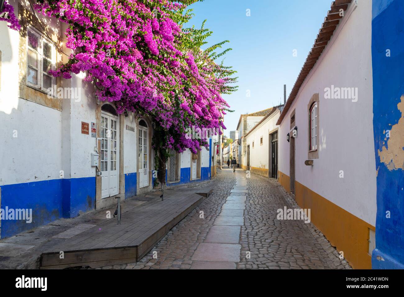 Malerische gepflasterte Fußgängerzone mit hellen violetten Bougainvillea in Obidos, Portugal, eine alte ummauerte Stadt Stockfoto