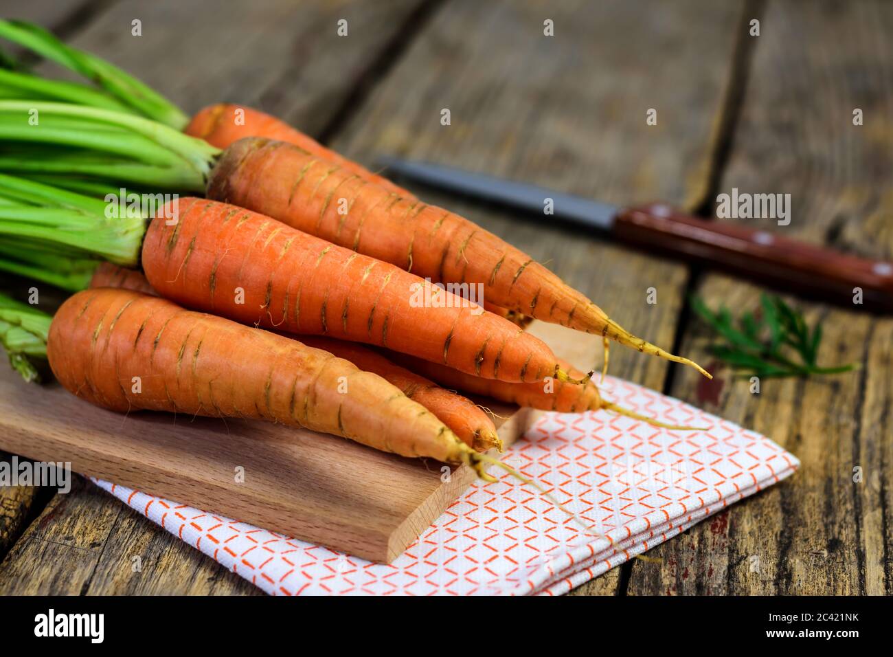 Frische Karotten auf einem Schneidebrett, Messer und Geschirrtuch auf altem Holztisch. Selektiver Fokus. Stockfoto