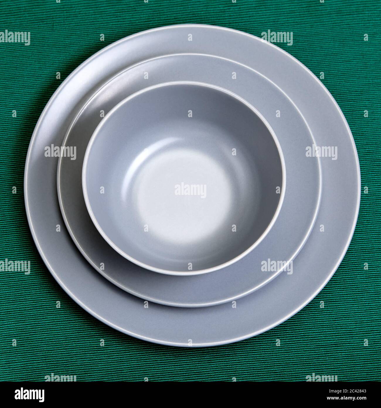 Set aus grau glasierten Keramikschalen in verschiedenen Größen und Formen, auf grünem Hintergrund. Küchenutensilien, Schüssel, Untertasse und Teller. Stockfoto