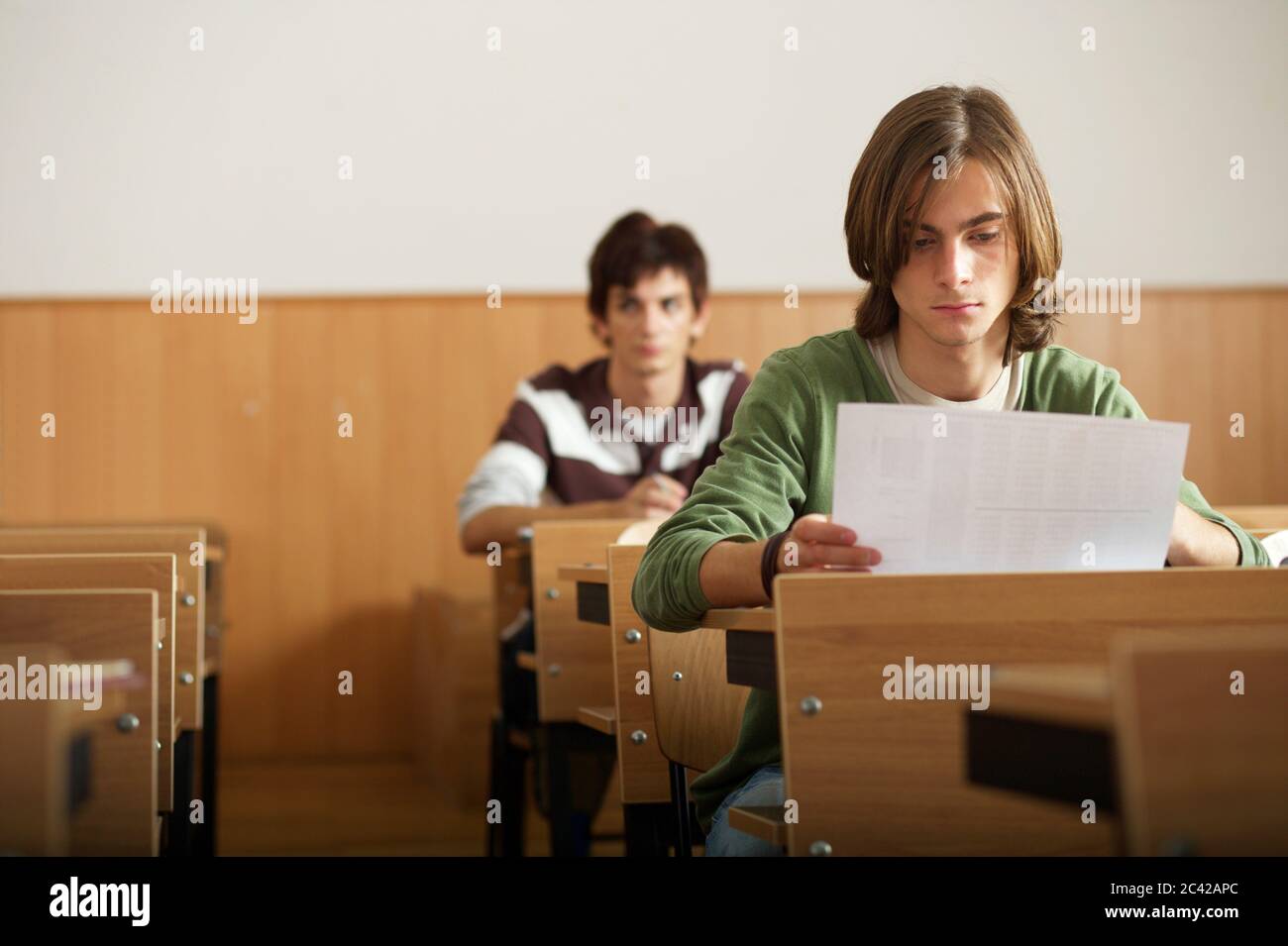 Junge mit mittellangen Haaren sieht sich Aufgaben - Klassenzimmer - Schüler - Prüfung Stockfoto