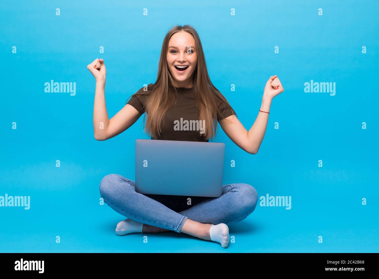 Emotionale junge Frau mit Laptop feiert Sieg auf farbigen Hintergrund Stockfoto