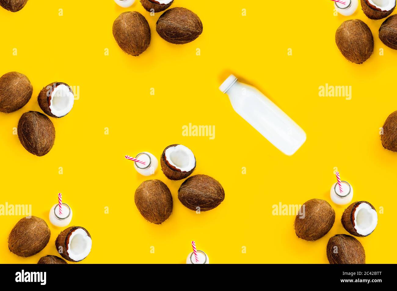 Muster mit reifen Kokosnüssen und Flasche mit Getränk auf gelbem Hintergrund. Draufsicht. Kreatives Sommerkonzept. Exotische und tropische Erfrischung. Natürlicher Plan Stockfoto