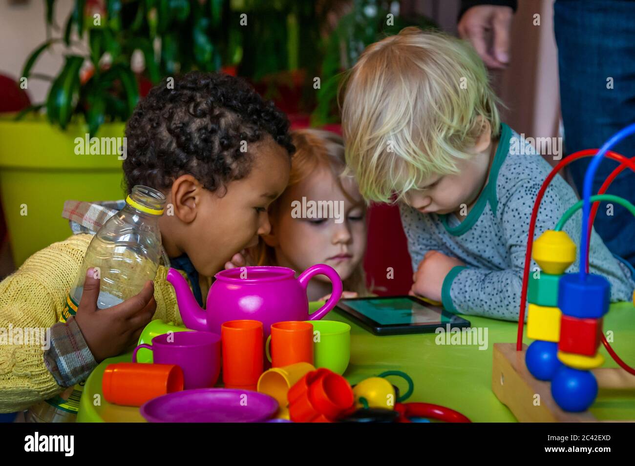 In einer Spielecke konzentrieren sich drei kleine Kinder auf ein Smartphone Stockfoto