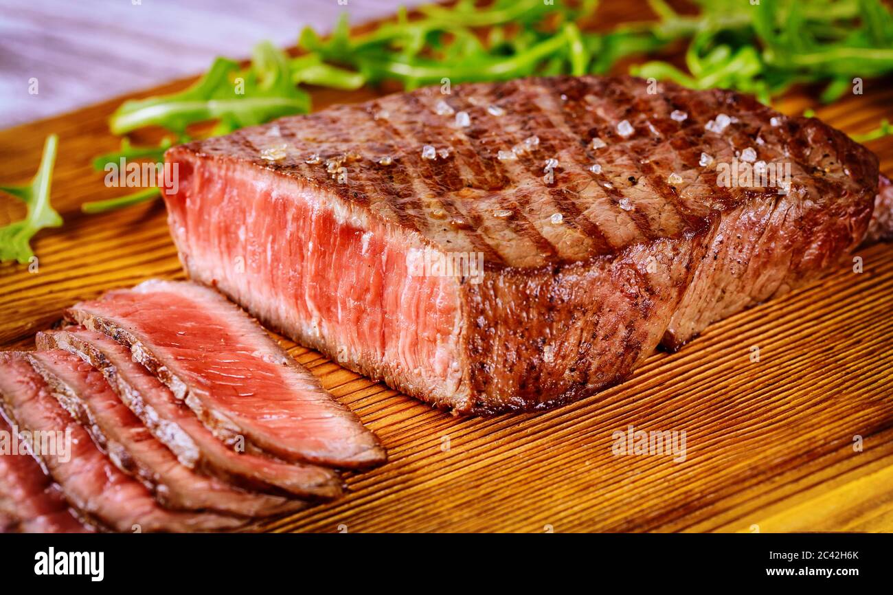 Köstliches und gesundes gegrilltes mittelseltenes Rindersteak auf Holzbrett mit Rucola. Stockfoto