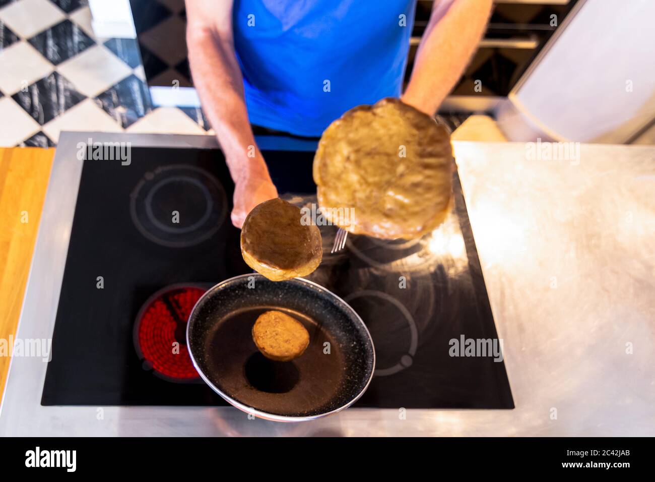 Mann Kochen hält eine Pfanne mit Seitan Burger fliegen in der Luft mit selektivem Fokus. Veganes Konzept Stockfoto