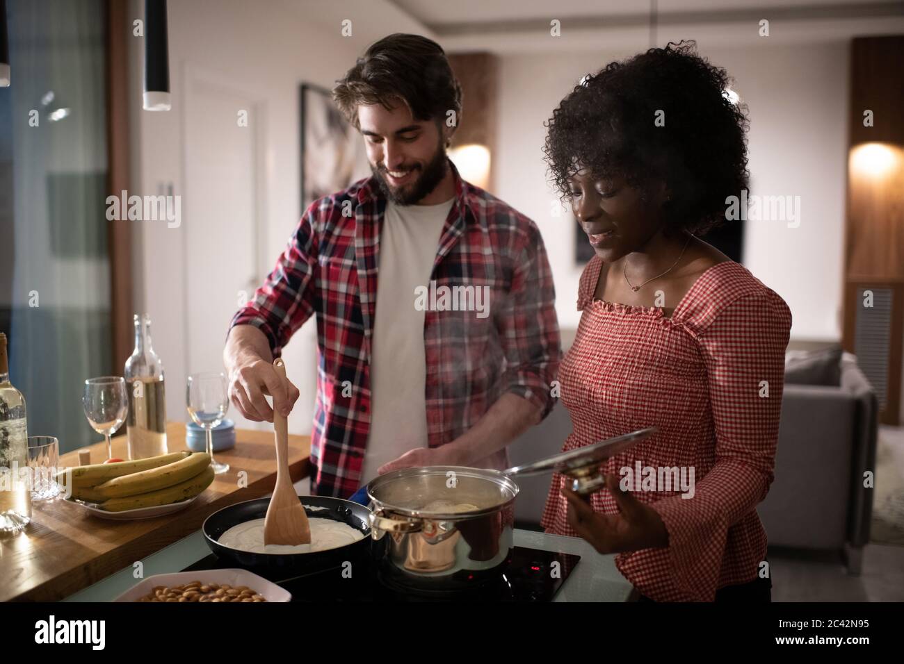 Glückliche multirassische Mann und Frau in lässigen Kleidern lächeln und kochen köstliche Gerichte zusammen vor dem romantischen Abendessen zu Hause Stockfoto