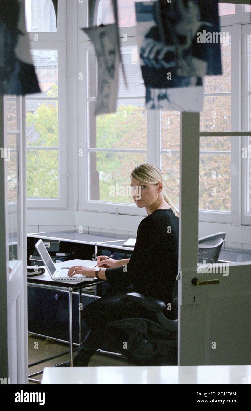 Junge blonde Frau mit Laptop am Schreibtisch - Büro Stockfoto