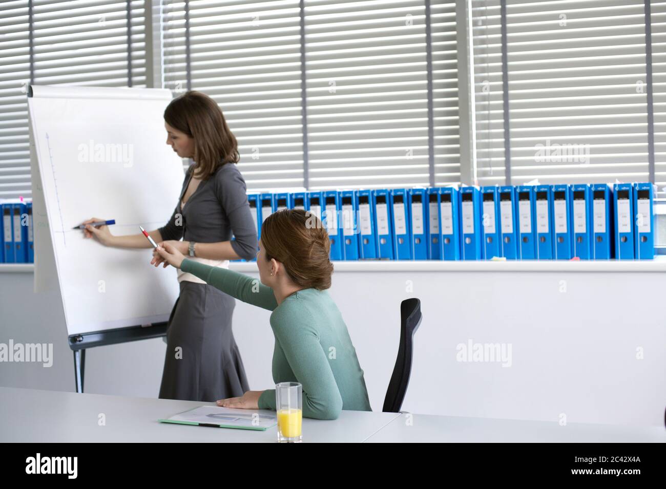 Junge Frau malt auf einem Flipchart - Büro-Ranking nach den Anweisungen ihres Chefs Stockfoto