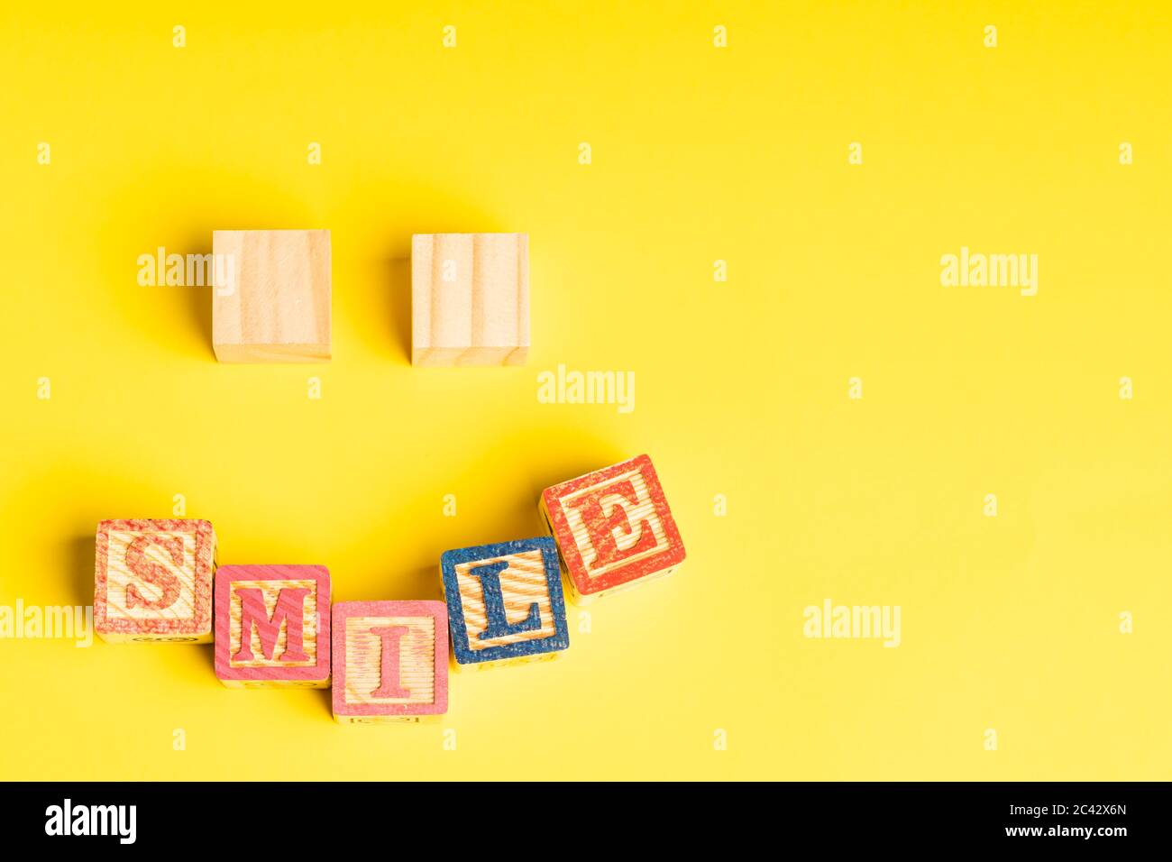 Holzblöcke bilden ein lächelndes Gesicht vor gelbem Hintergrund mit Copy Space für Text Stockfoto