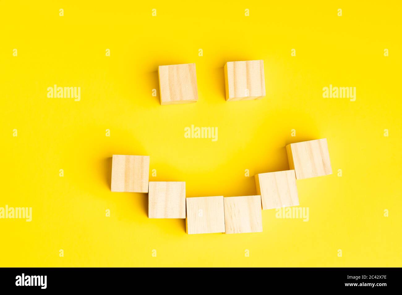 Holzblöcke bilden ein lächelndes Gesicht vor gelbem Hintergrund mit Copy Space für Text Stockfoto