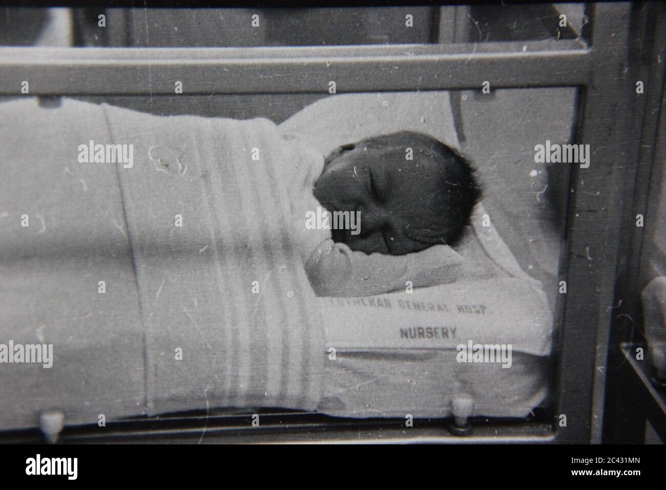 Schöne Schwarz-Weiß-Fotografie eines neugeborenen Babys in der Entbindungsstation des Krankenhauses, das versucht, in seiner Krippe zu schlafen. Stockfoto