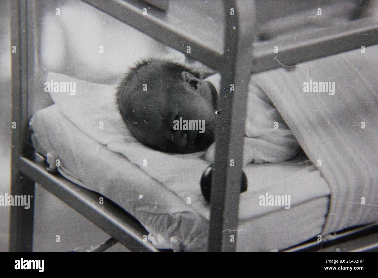 Schöne Schwarz-Weiß-Fotografie eines neugeborenen Babys in der Entbindungsstation des Krankenhauses, das versucht, in seiner Krippe zu schlafen. Stockfoto