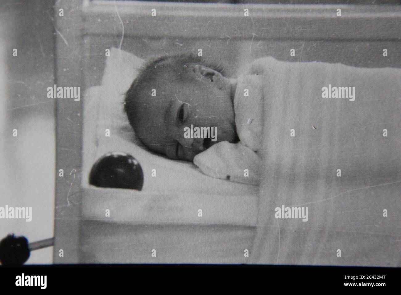 Schöne Schwarz-Weiß-Fotografie eines neugeborenen Babys in der Entbindungsstation des Krankenhauses, das versucht, in seiner Krippe zu schlafen. Stockfoto