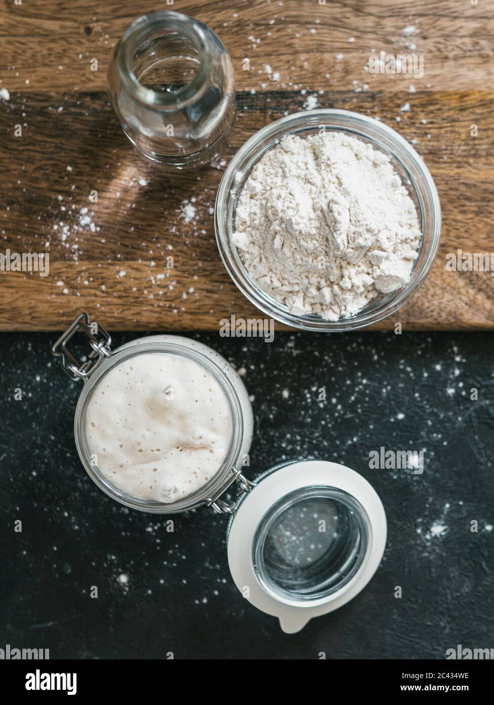 Vorspeise mit Weizensauerteig. Ansicht von oben auf Glas mit Sauerteig Starter, Wasserflasche und Weizenmehl Stockfoto