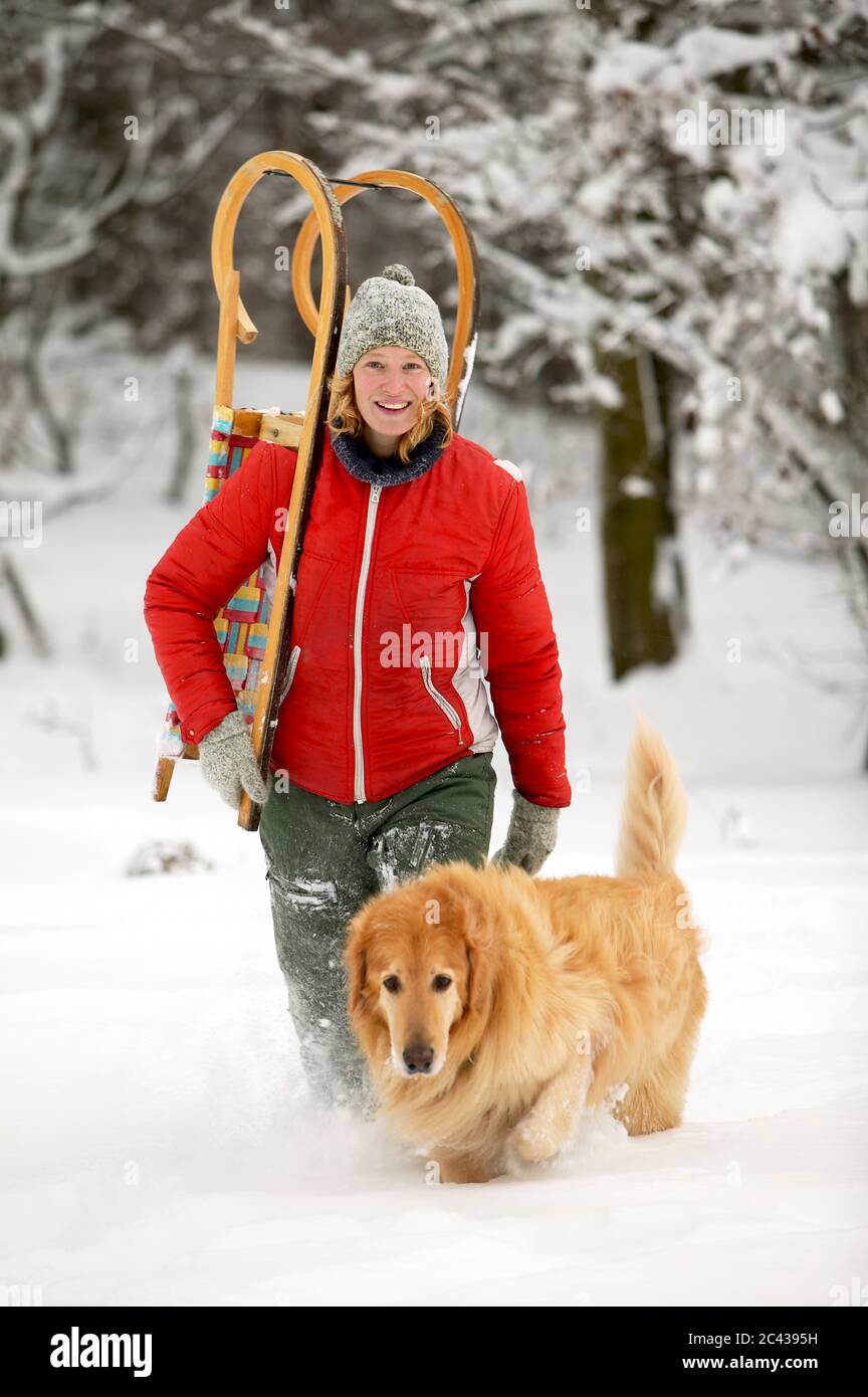 Frau trägt Schlitten Huckepack, läuft durch den Schnee mit einem Hund Stockfoto