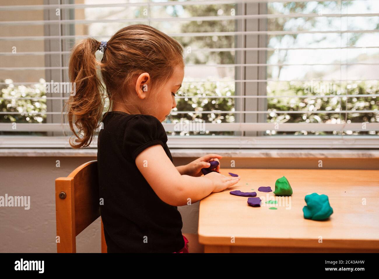 Nahaufnahme eines Kindes, das mit Spielteig in einem Spielzimmer auf einem Holztisch spielt. Mädchen modellieren Ton. Kind spielt und kreiert aus Spielteig. Stockfoto