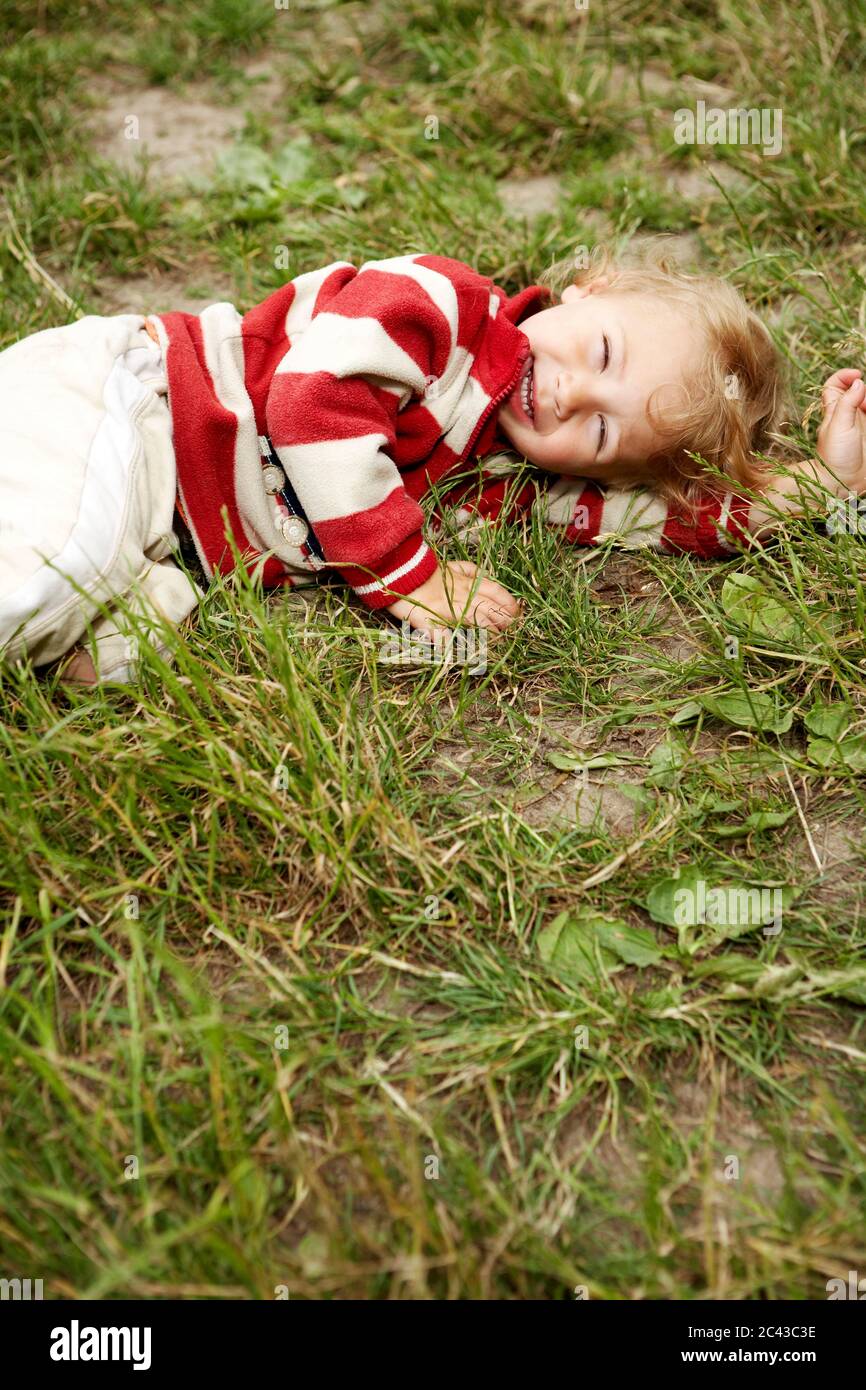 Lachender Junge (2-3 Jahre) liegt auf einer Wiese Stockfoto