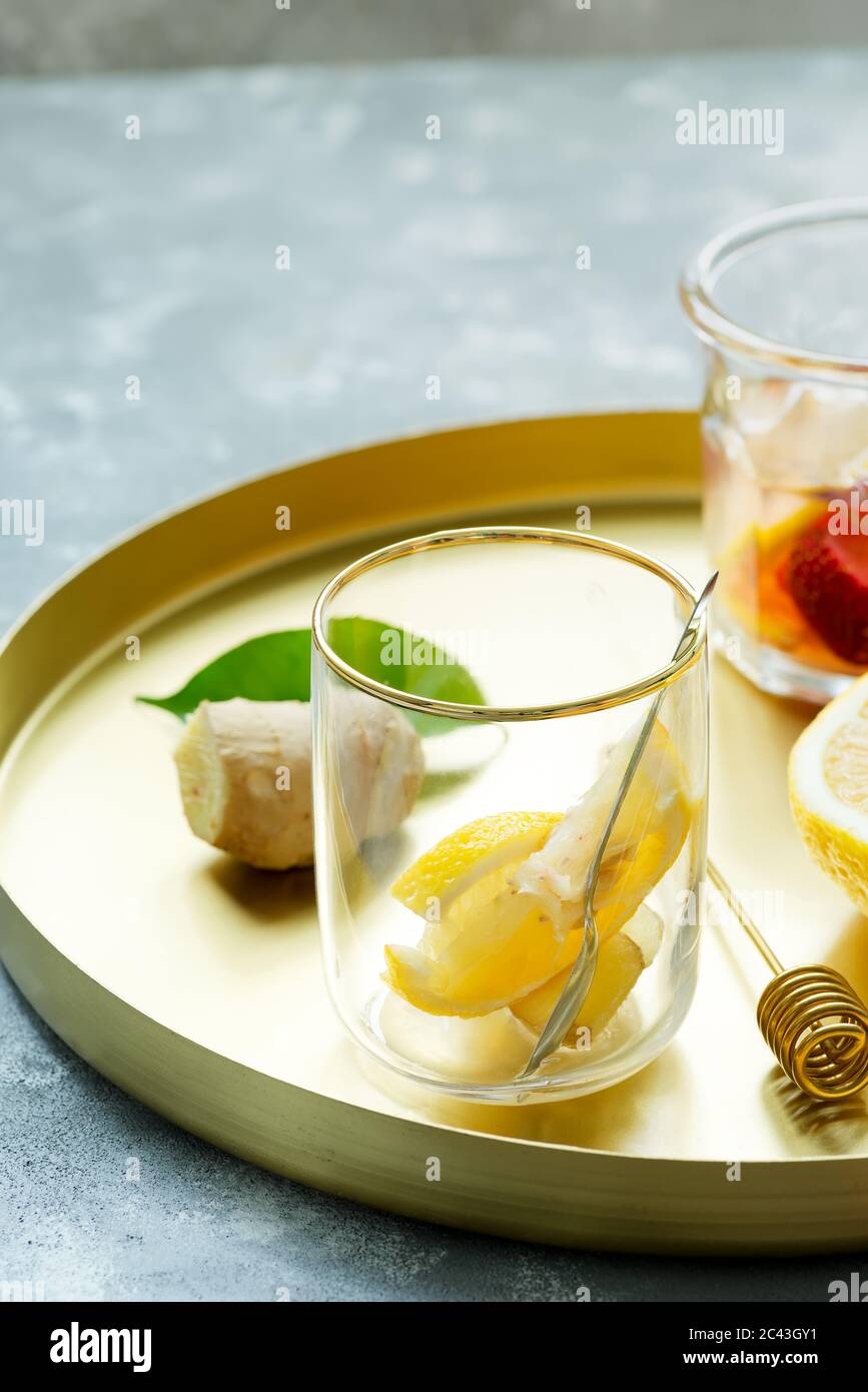 Rundes goldenes Tablett mit hausgemachter erfrischender kalter Limonade oder Cocktail aus natürlichem Ingwer und Zitronenfrüchten in Gläsern auf einem grauen Tisch, Kopierplatz. Kalt Stockfoto