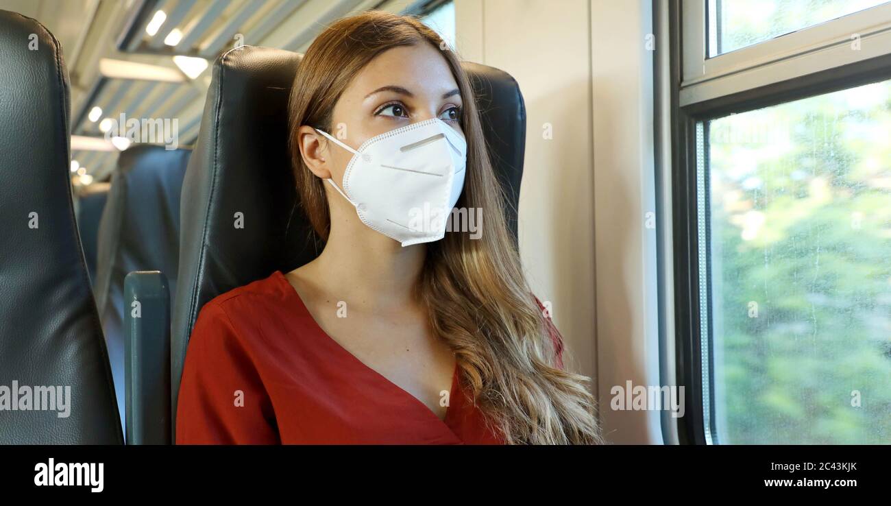 Sicher mit öffentlichen Verkehrsmitteln reisen. Junge Frau mit KN95 FFP2 Gesichtsmaske Blick durch Zug Fenster. Zug Passagier mit Schutzmaske reist sitzen Stockfoto