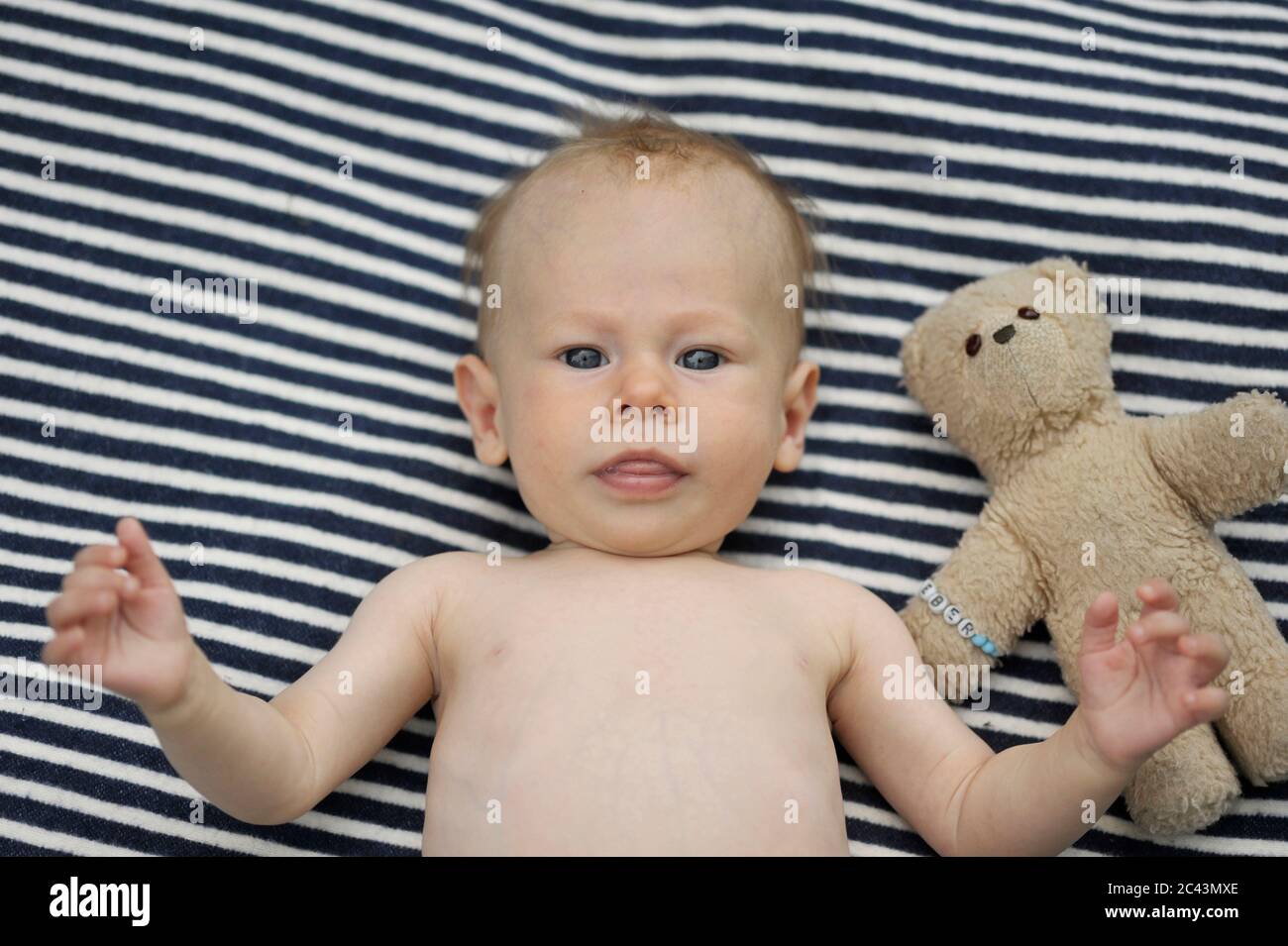 Baby liegt auf einer Decke mit einem Teddybär Stockfoto
