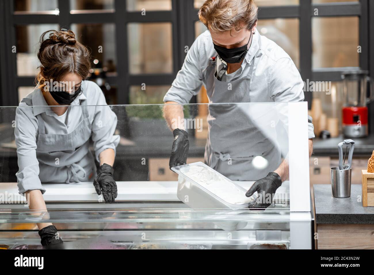 Zwei Verkäufer in Masken und Handschuhen, die in der Eisdiele oder im Café arbeiten. Konzept neuer Regeln für Unternehmen während einer Pandemie Stockfoto