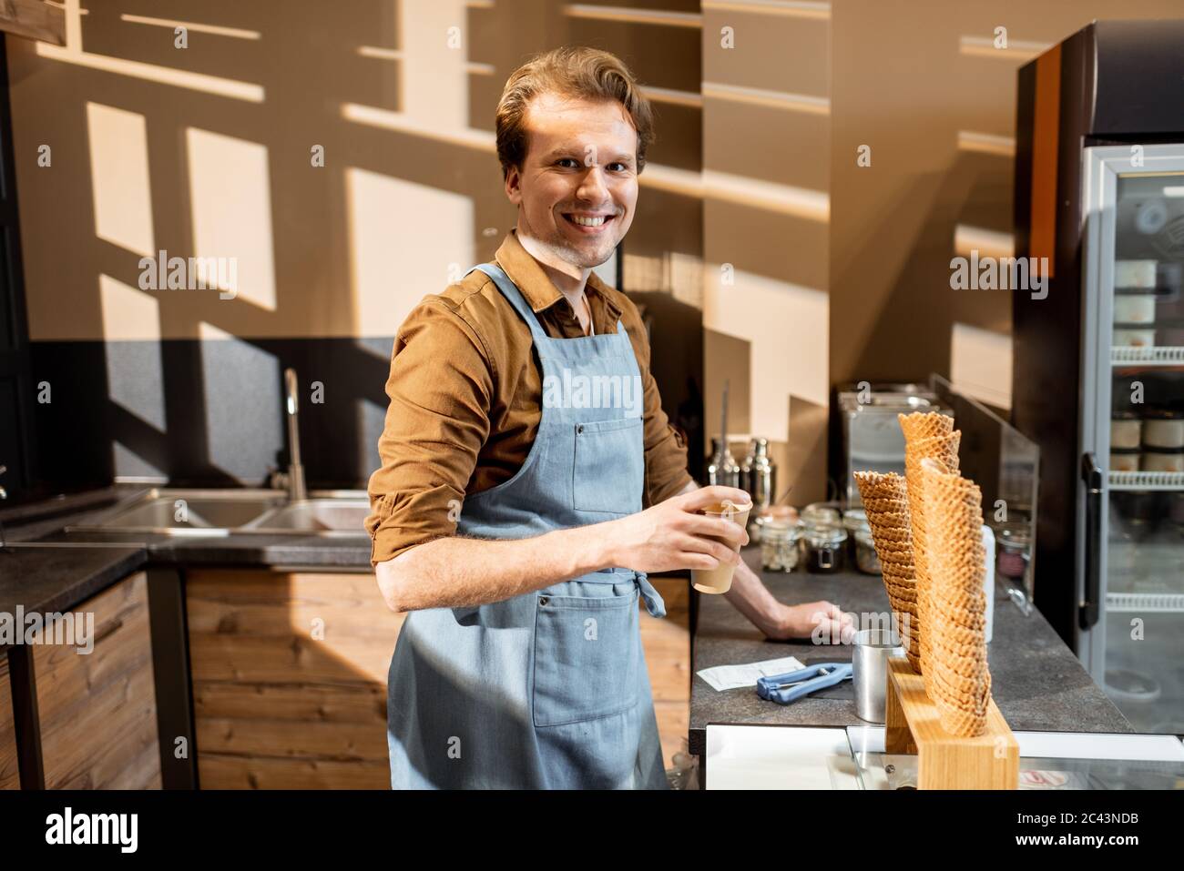 Porträt eines fröhlichen Verkäufers oder Geschäftsinhabers in Schürze gekleidet, der an der Theke einer Konditorei oder eines Cafés steht Stockfoto