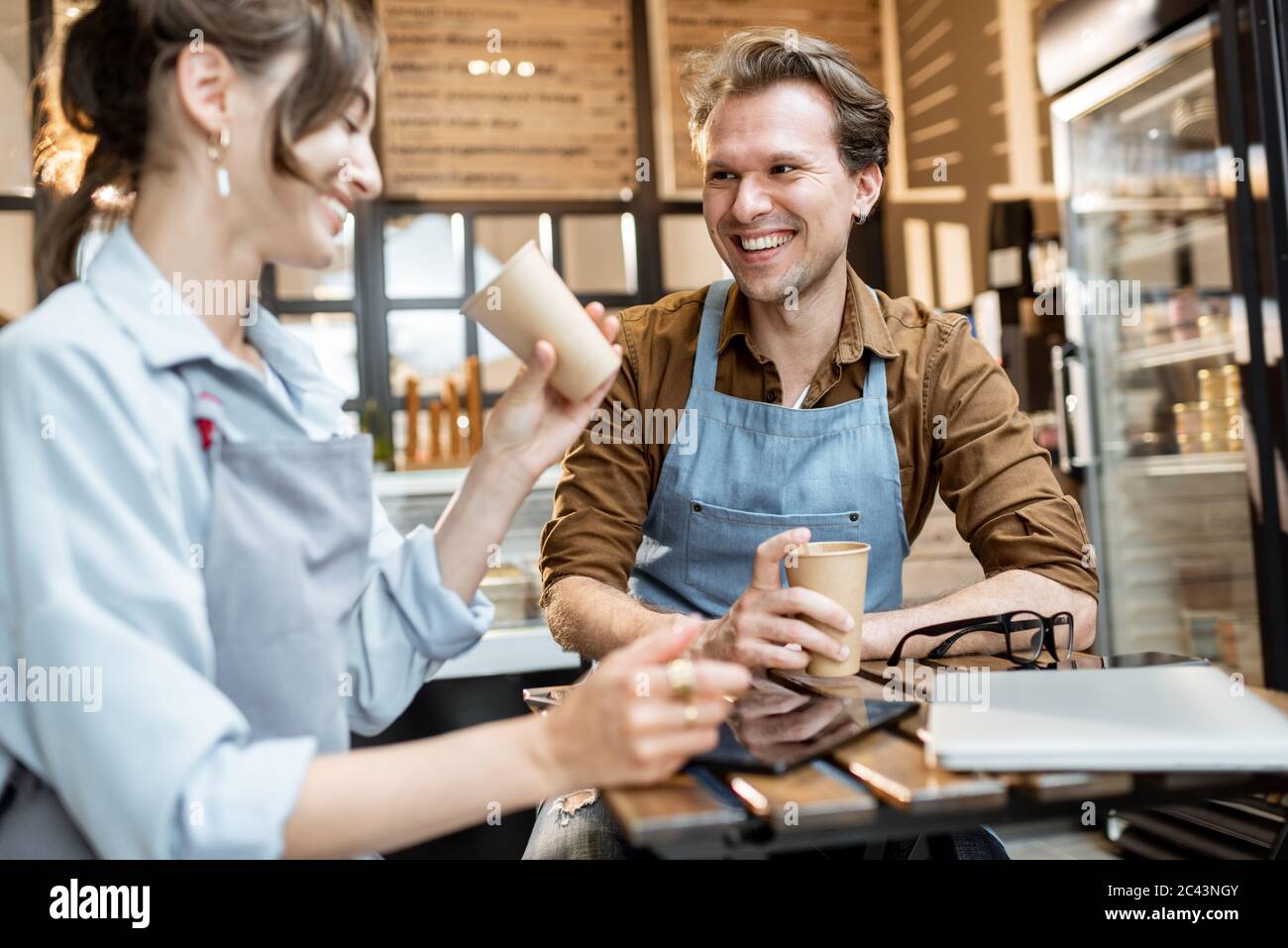 Ein paar junge Cafe-Arbeiter haben einige Geschäftsgespräche, während sie mit Kaffee am Tisch ihres Cafés oder Konditorei sitzen Stockfoto