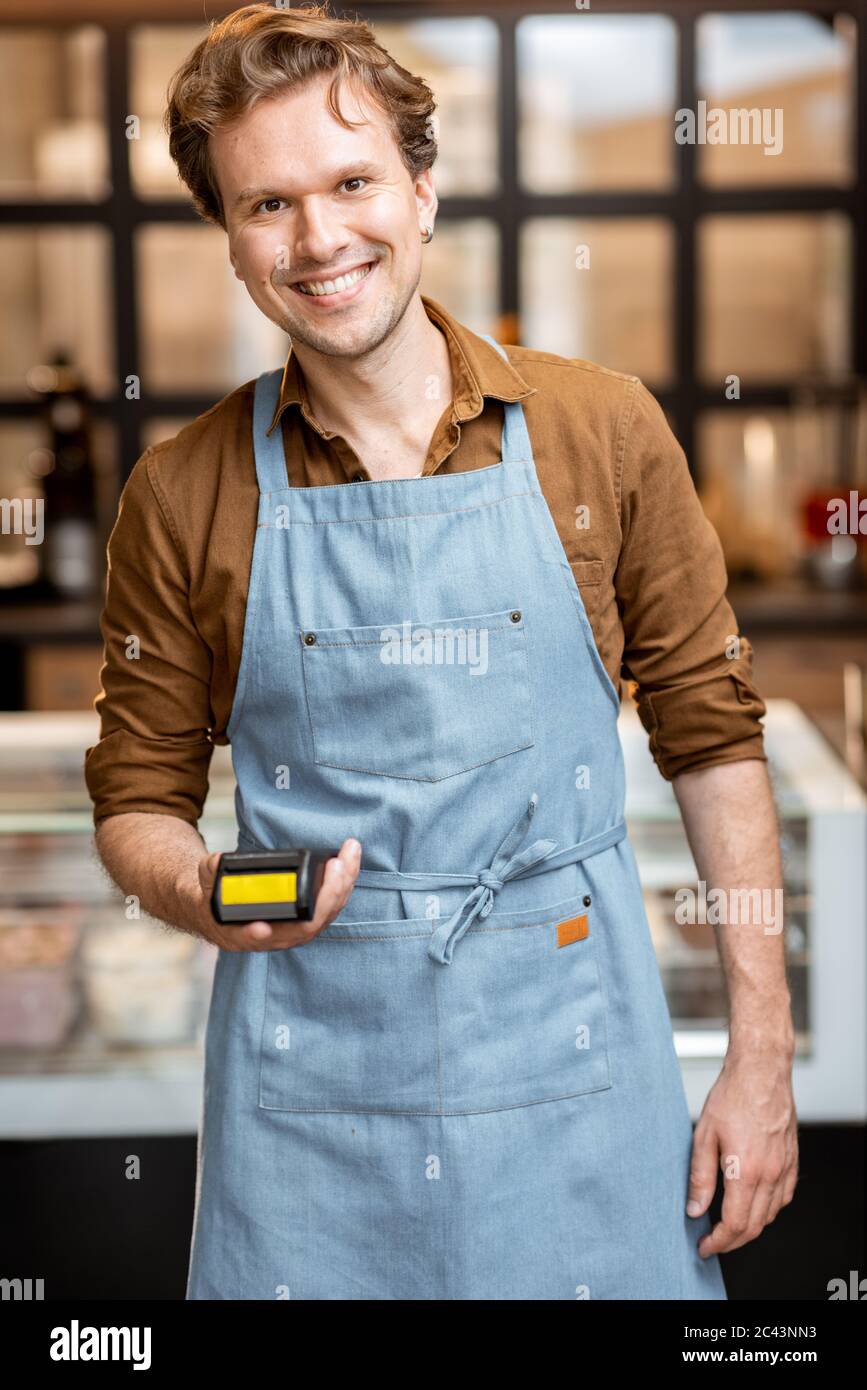 Porträt eines fröhlichen Kellners, der mit einem Bankterminal für eine Zahlung im Café oder kleinen Laden steht Stockfoto