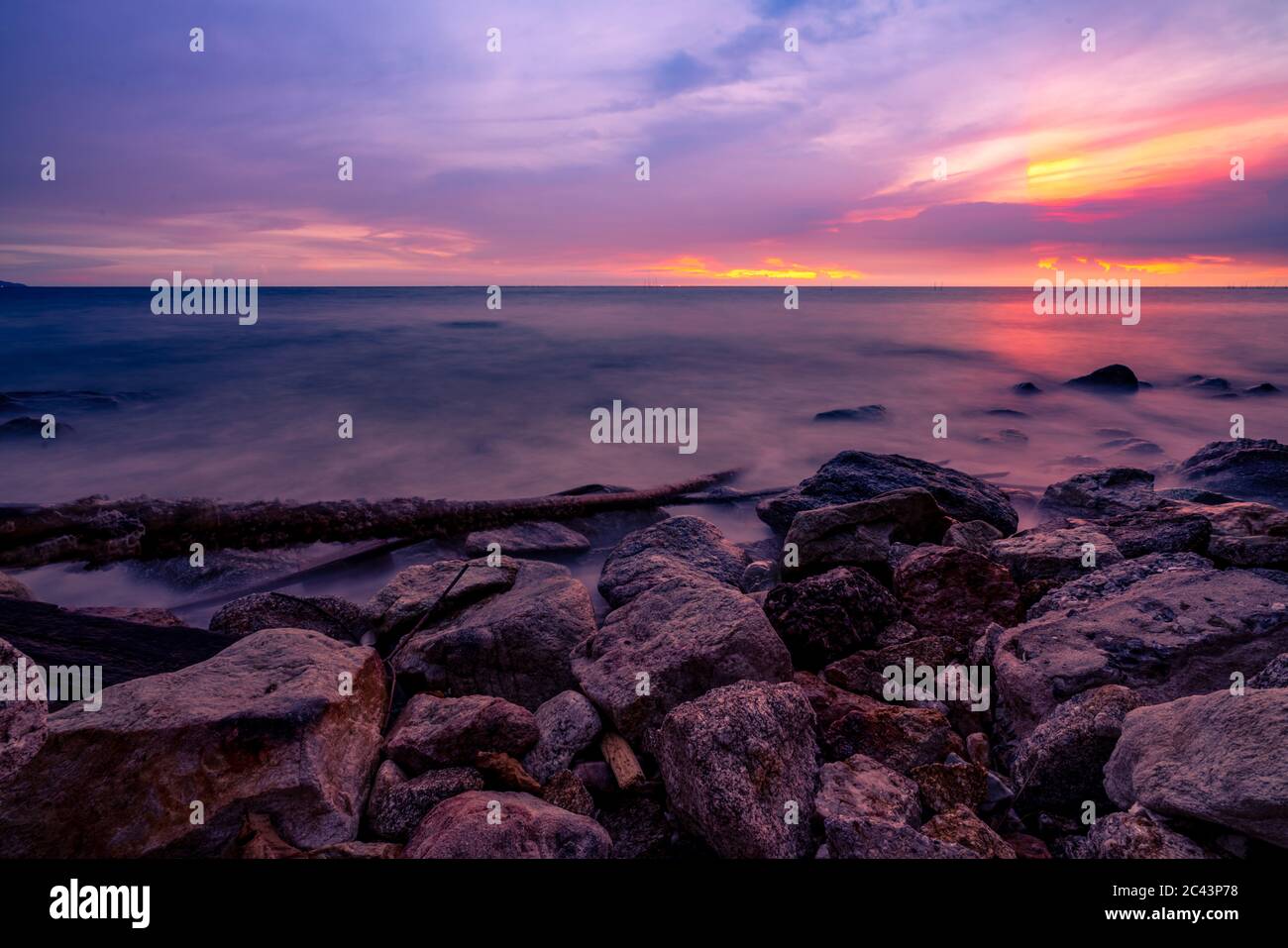 Steinstrand und ruhiges Meer bei Dämmerung mit purpurem Sonnenuntergang Himmel. Tropisches Meer. Skyline am Abend mit goldenem, purpurem und rotem Himmel. Meereslandschaft. Sommer. Stockfoto
