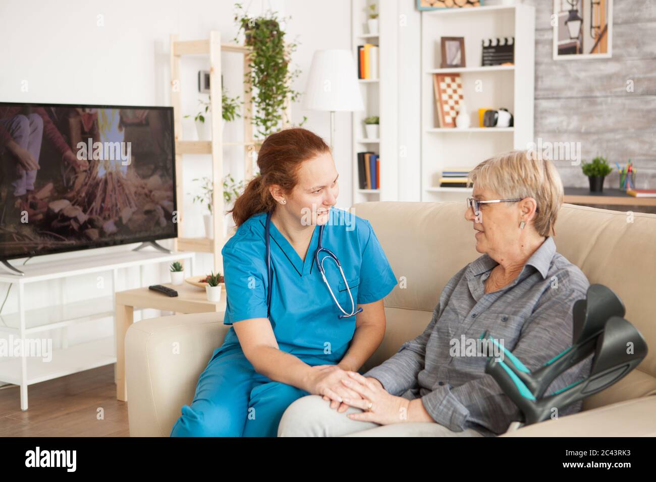 Assistentin im Gespräch mit älteren Frau im Pflegeheim mit Krücken. Stockfoto