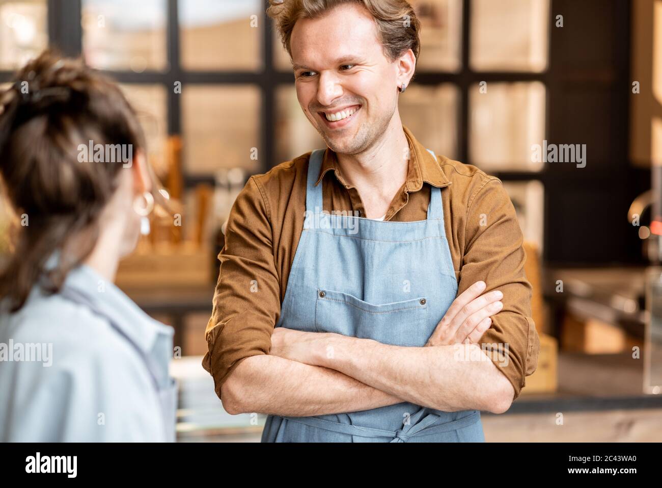 Porträt von zwei fröhlichen Mitarbeitern eines Cafés oder kleinen Ladens, die vor der Theke im Inneren stehen Stockfoto