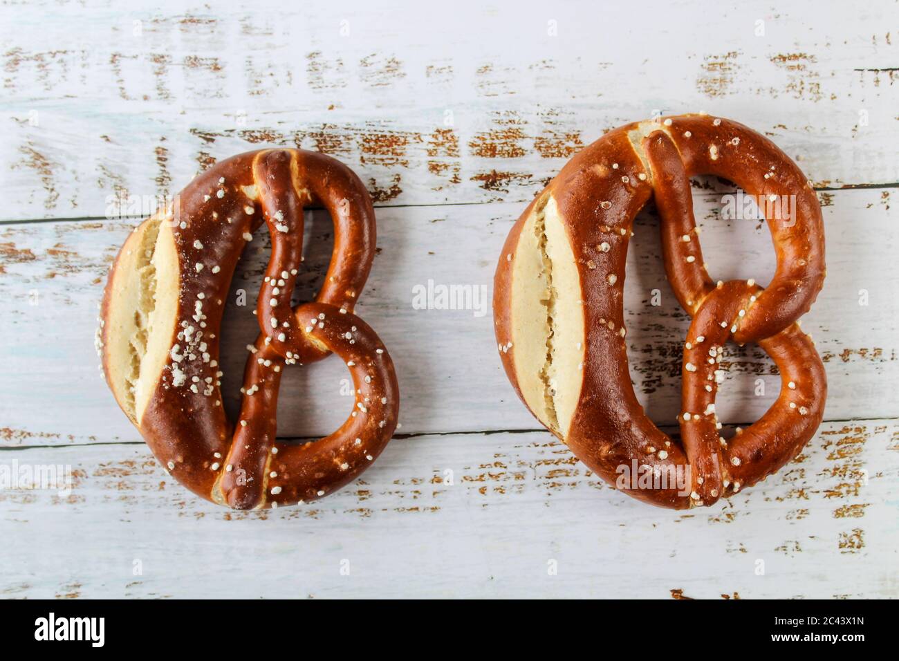 Frisch gebackene bayerische Brezel mit Salz auf rustikalem weißen Tisch. Perfekt für Oktoberfest. Nahaufnahme von hausgemachten Brezeln mit dunkler Kruste. Stockfoto