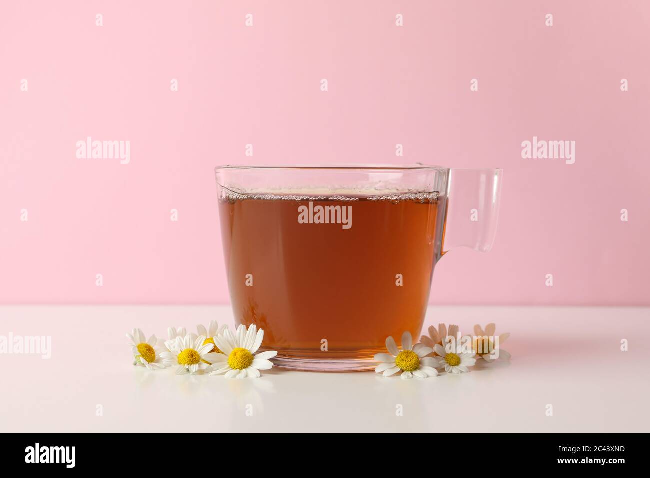 Tasse Tee und Kamille auf weißem Tisch vor rosa Hintergrund Stockfoto