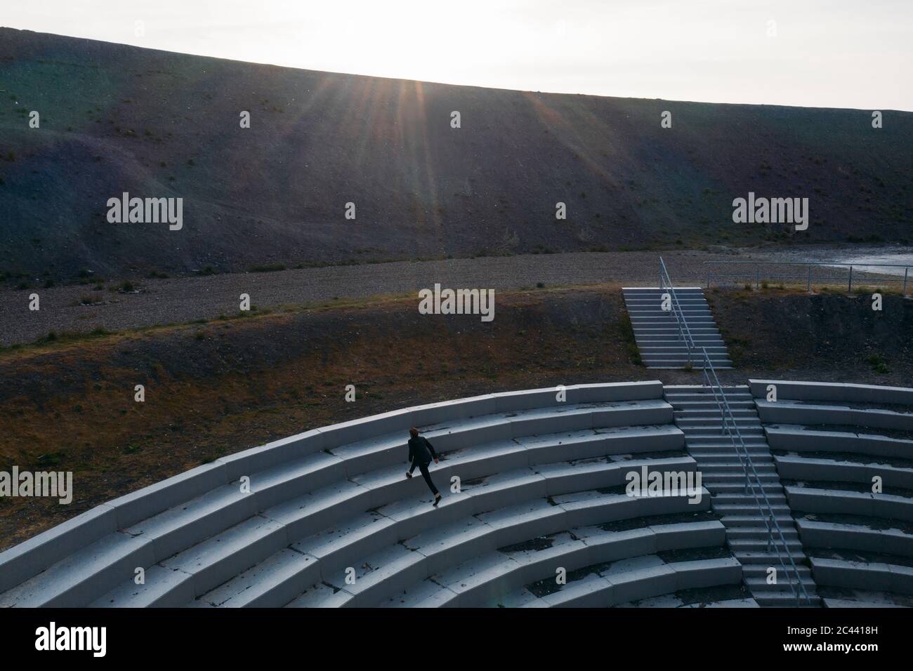 Geschäftsmann, der bei Sonnenuntergang auf die Stufen der BergArena aufsteigen kann Stockfoto